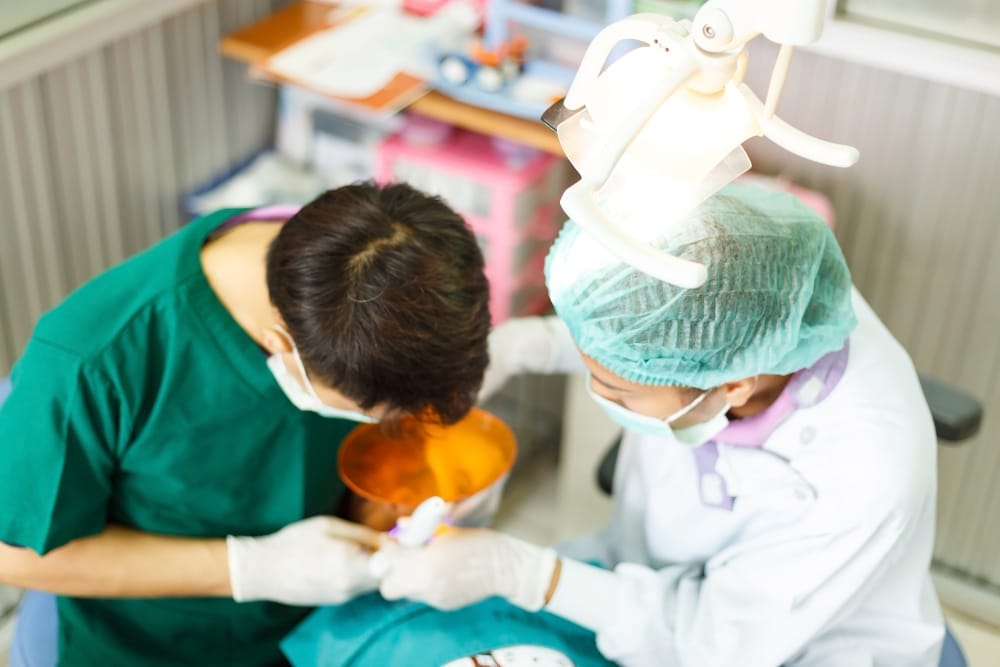 A dentist and an assistant performing a dental procedure on a patient under a bright overhead light.