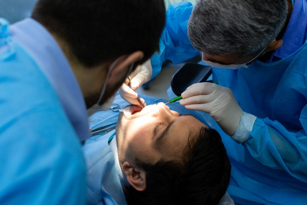 A patient lying in a dental chair with two dentists performing a dental procedure using instruments.