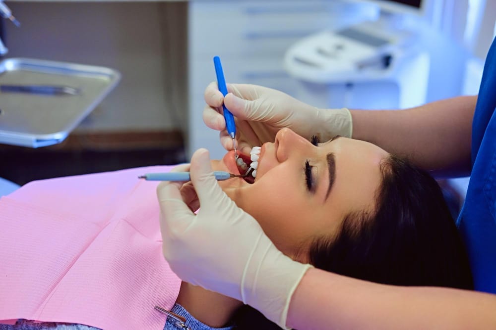 A dentist in a white coat and gloves works on a patient's teeth during a cosmetic dental treatment. The patient is relaxed in the dental chair, while the dentist carefully applies a dental tool to enhance the appearance of the patient's smile.